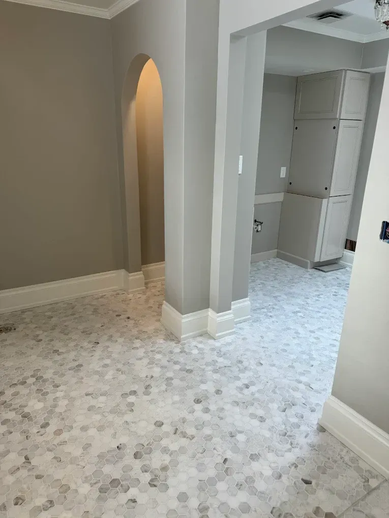 Room with gray and white hexagon tile floor, gray walls, archway, and white cabinets.
