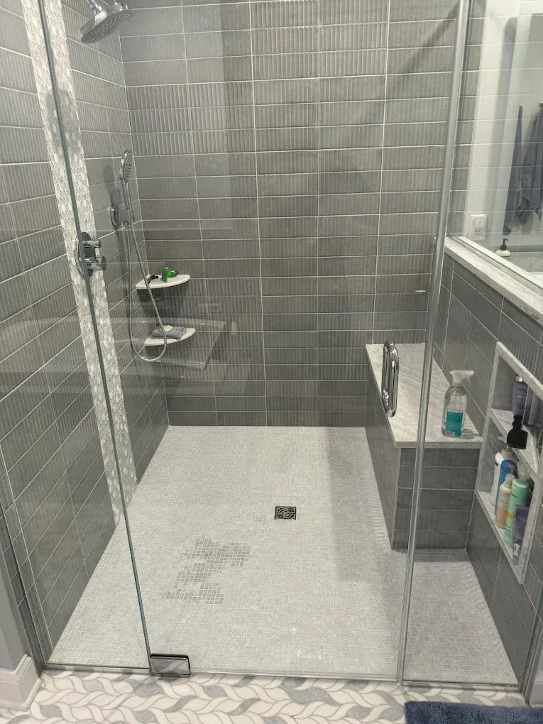 Gray tiled walk-in shower with glass doors, built-in bench, and recessed shelves.
