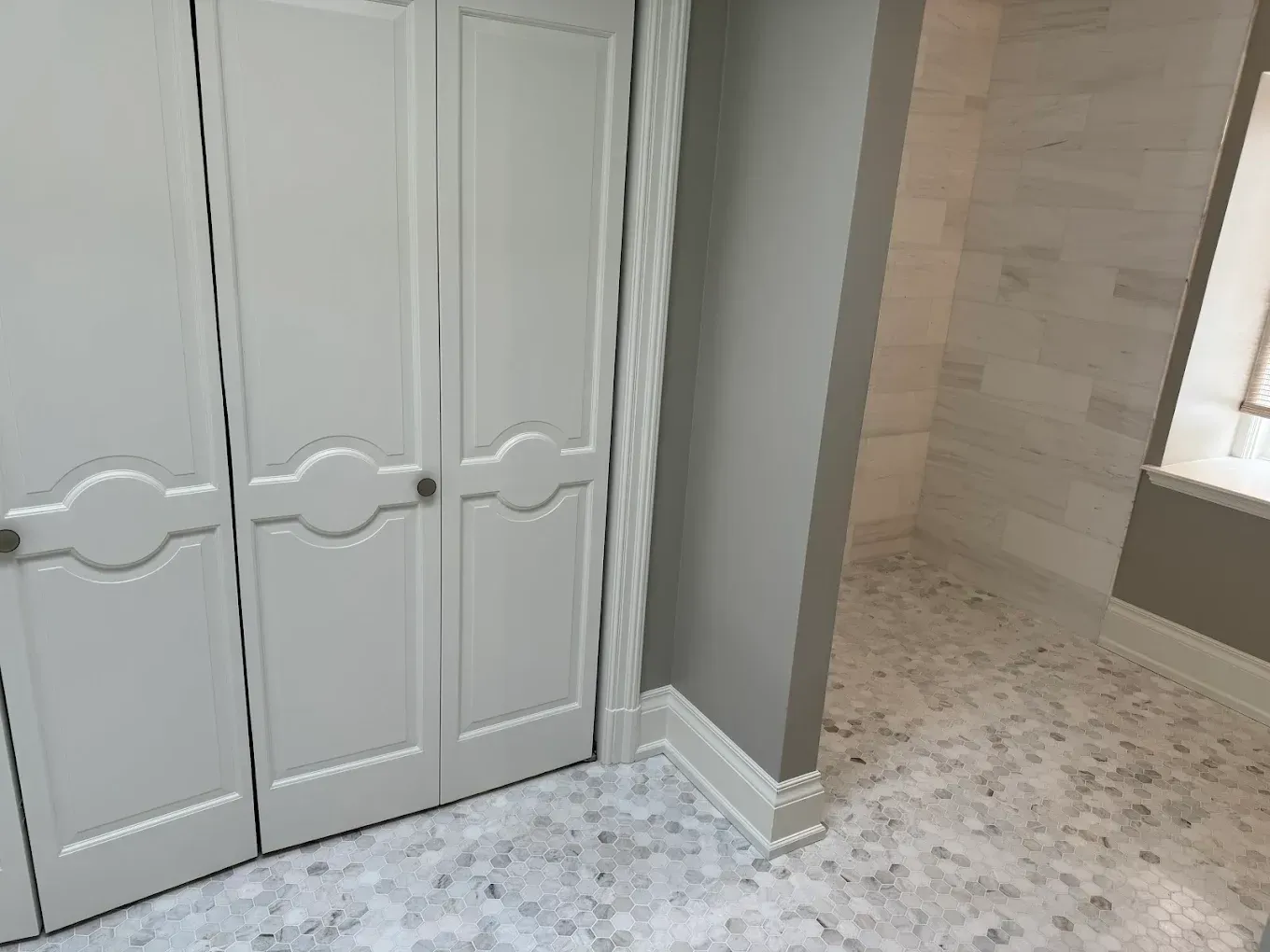 White closet doors next to a gray-walled bathroom with stone tile flooring and shower.
