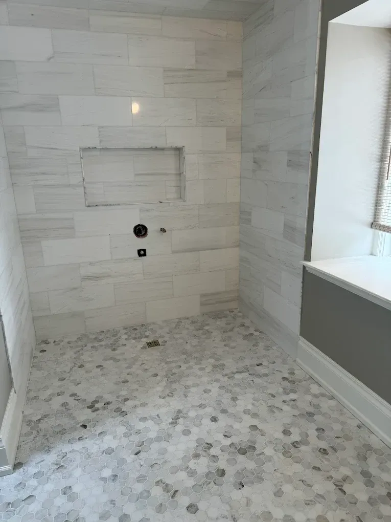 Shower with white marble tiled walls, a floor with small hexagonal tiles, and a recessed shelf.