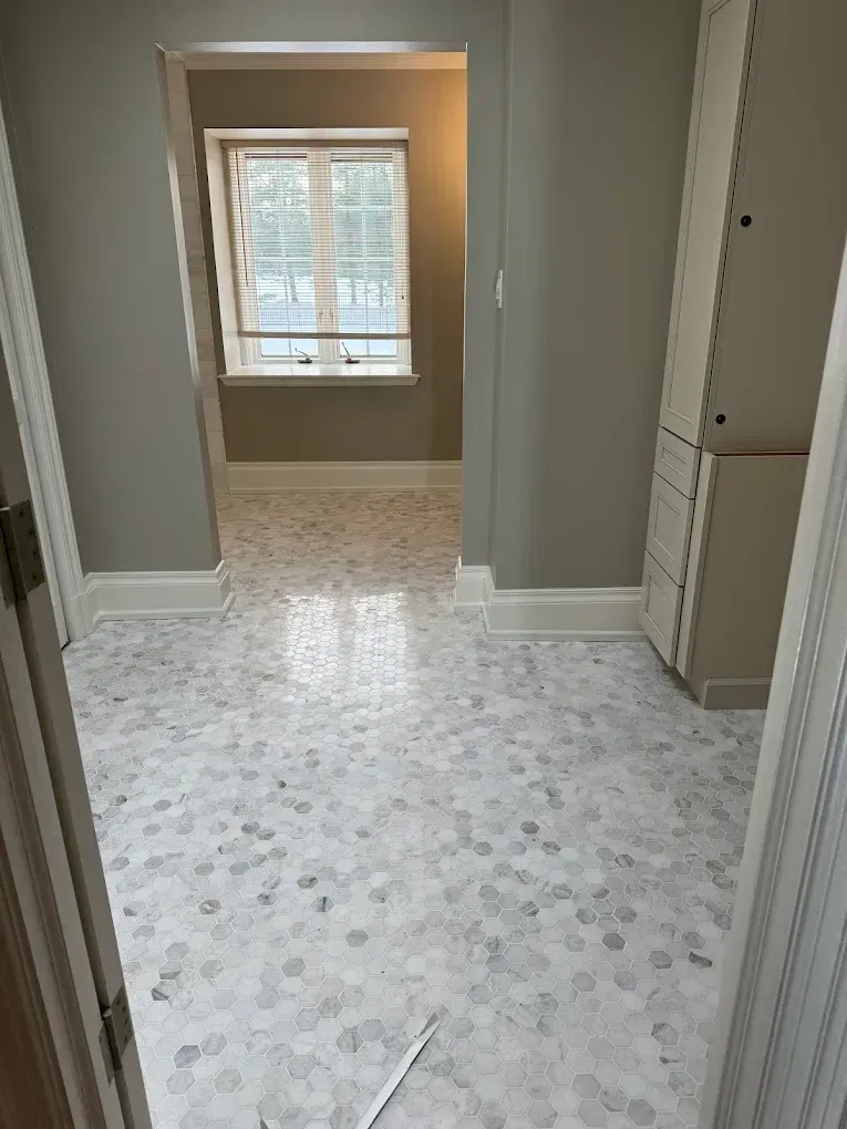 Hallway with gray walls, white baseboards, and mosaic tile flooring. A window at the end.