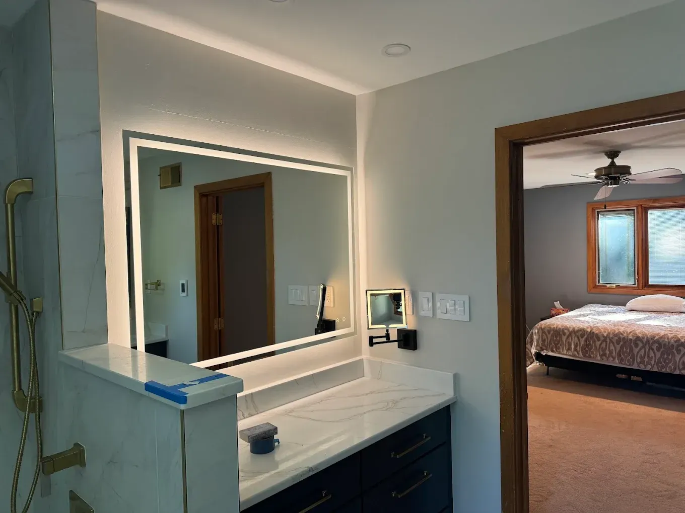 Bathroom with backlit mirror, vanity, and a view into a bedroom with a bed.
