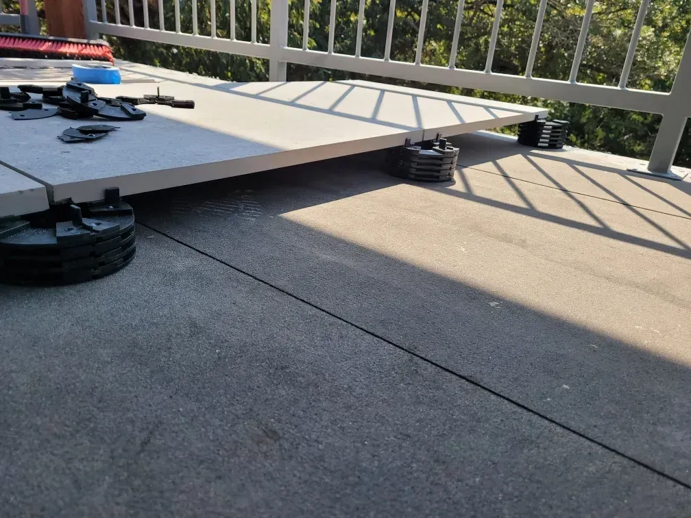 A deck tile partially installed on adjustable supports, sunlight casts shadows.