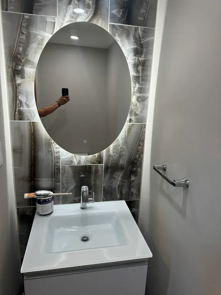 Modern bathroom with a white sink, oval mirror, and dark tile backsplash.