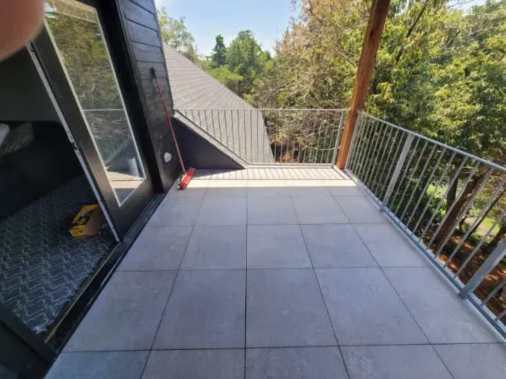 Balcony with gray tiled floor, metal railing, and view of trees.