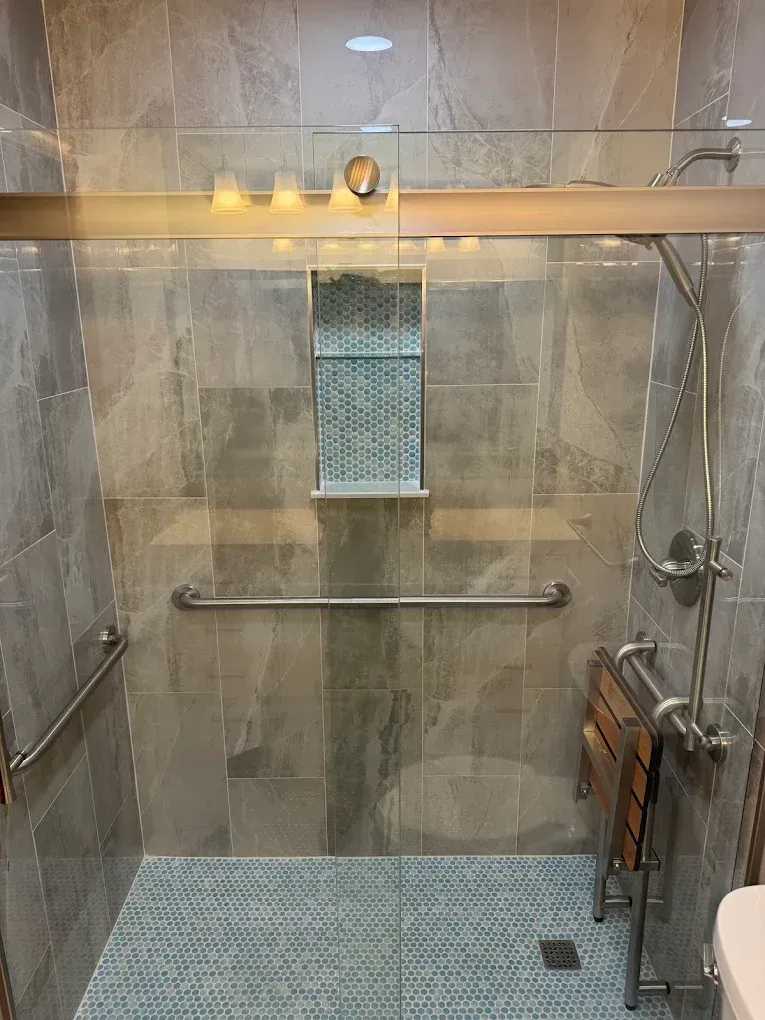 Accessible shower with grab bars, fold-down seat, and gray tile.