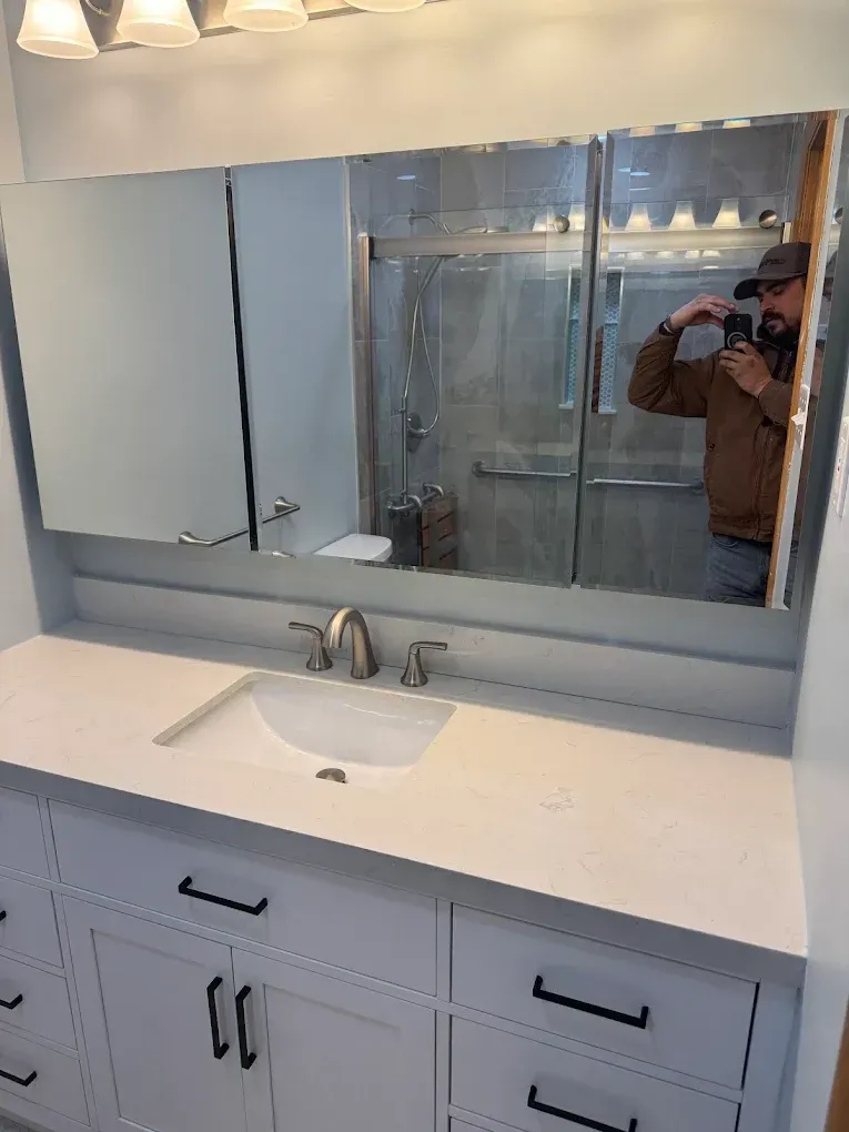 Bathroom with white vanity, sink, and mirror, featuring a person taking a photo.