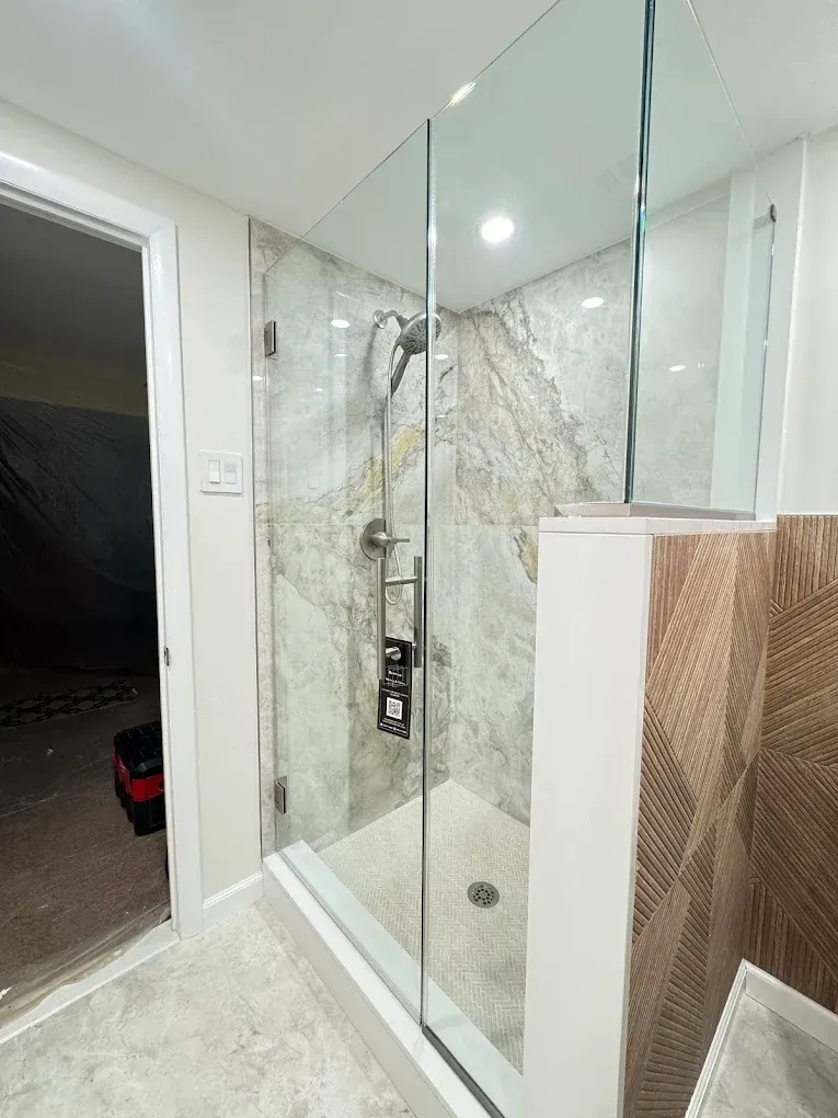 A modern shower with glass walls and light-colored stone tiling.