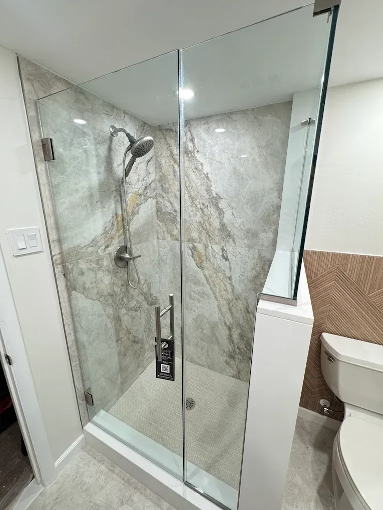 Glass shower with stone tile walls, silver fixtures, and small mosaic floor tiles. Toilet visible on the right.