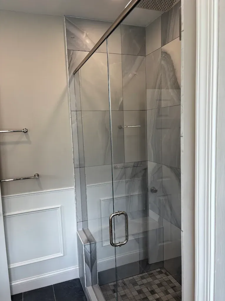 Bathroom shower with glass door and tile walls. Towel rack on the left.