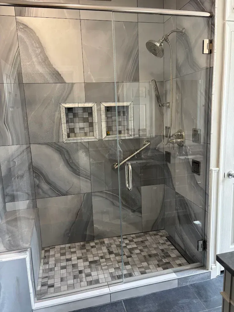 Shower with clear glass doors, gray tiled walls and floor, and chrome fixtures.