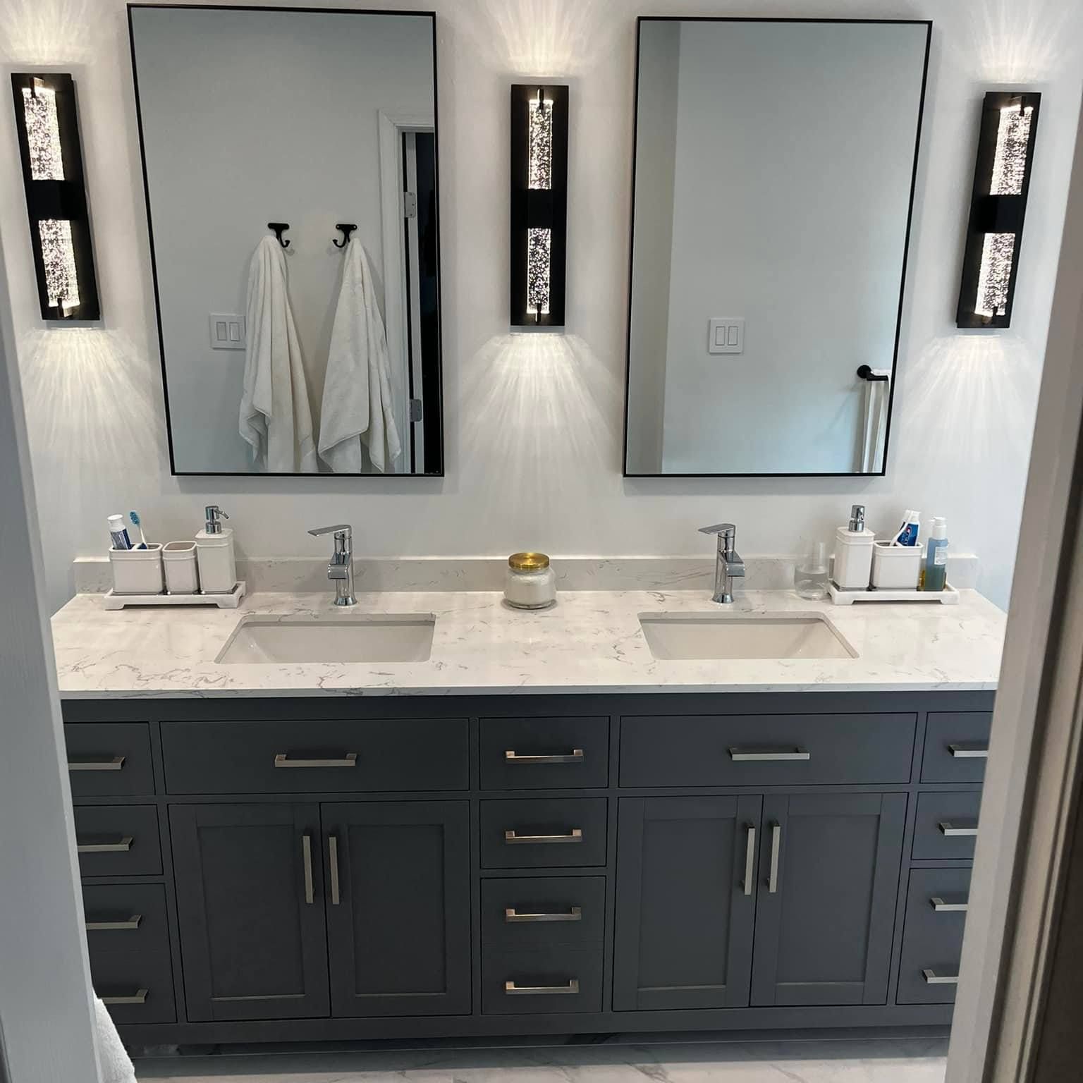 Bathroom with dual sinks, gray cabinets, two mirrors, sconces, and white countertop.