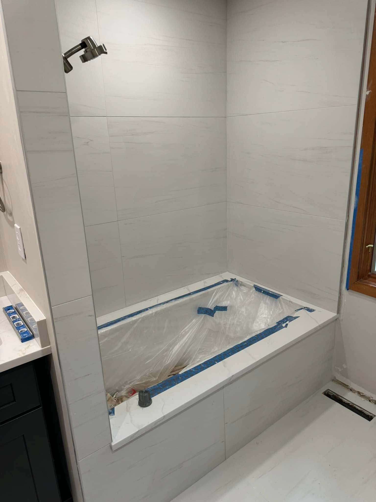 Bathroom with white tiled shower and tub, unfinished.