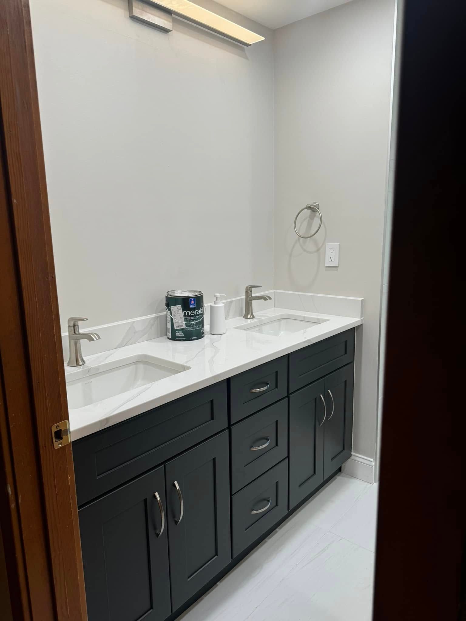 Bathroom with two sinks, dark cabinets, white countertop and walls, and light-colored floor.