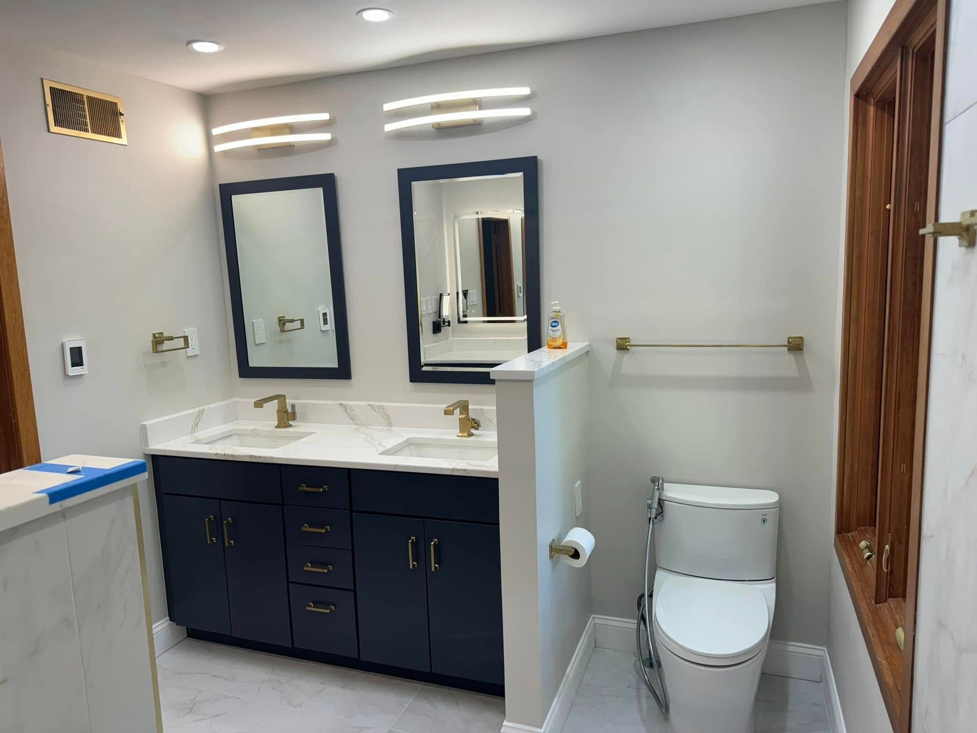Bathroom with navy vanity, white countertop, gold fixtures, and two mirrors.