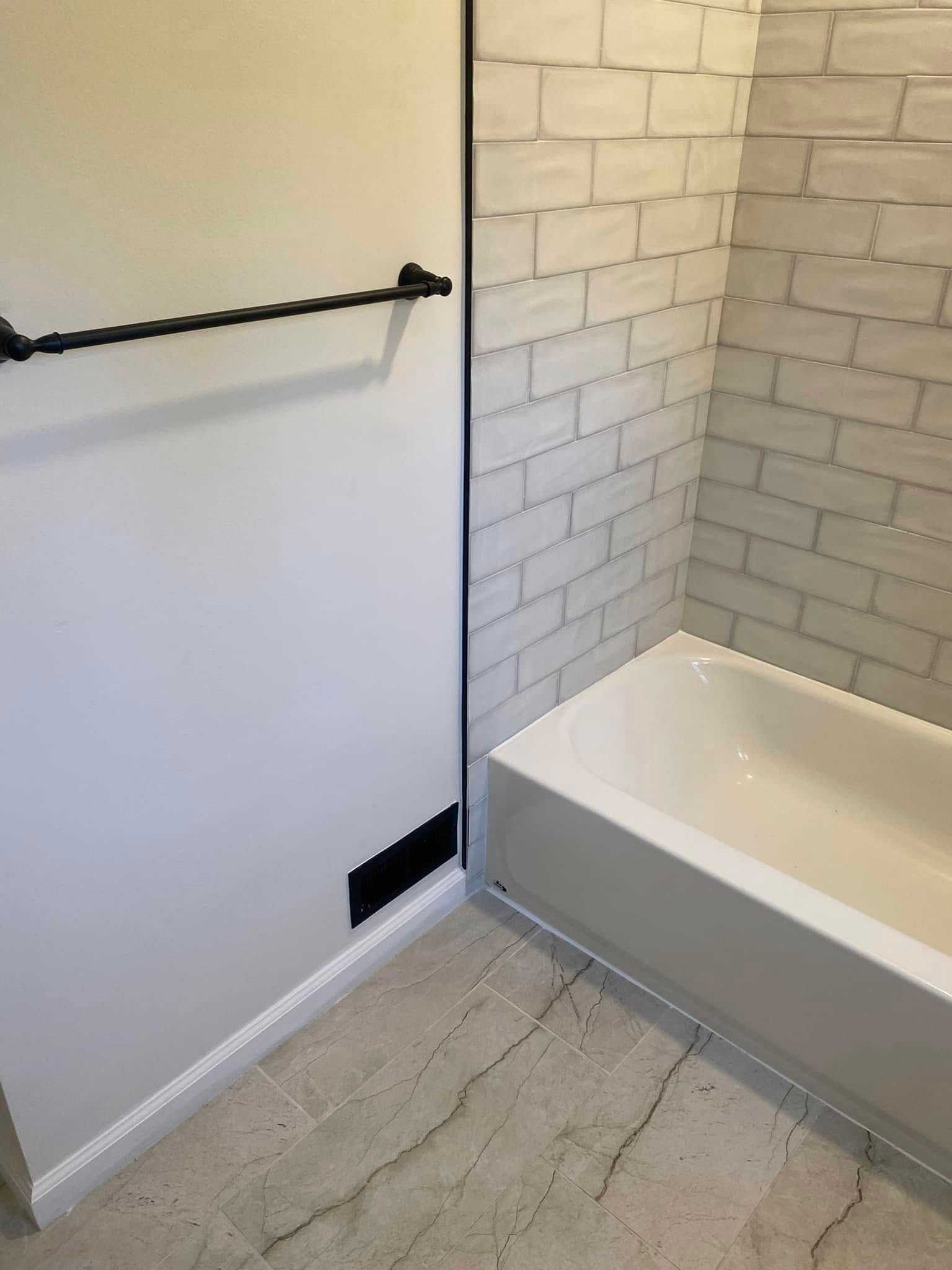 Bathroom with white tub, brick-like tile, towel rack, and vent on a white wall.