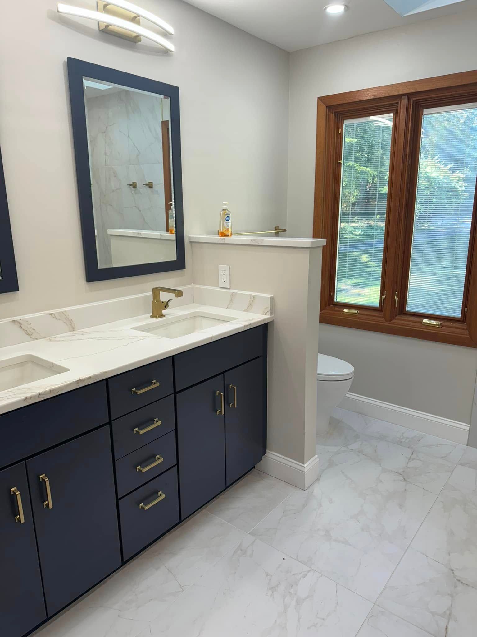 Navy blue vanity with gold hardware, white countertop, and rectangular mirror in a modern bathroom.