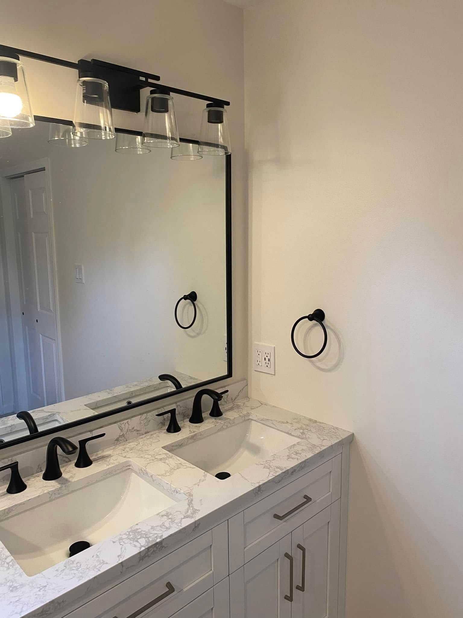 Bathroom vanity with double sinks, large mirror, black fixtures, and white cabinet.
