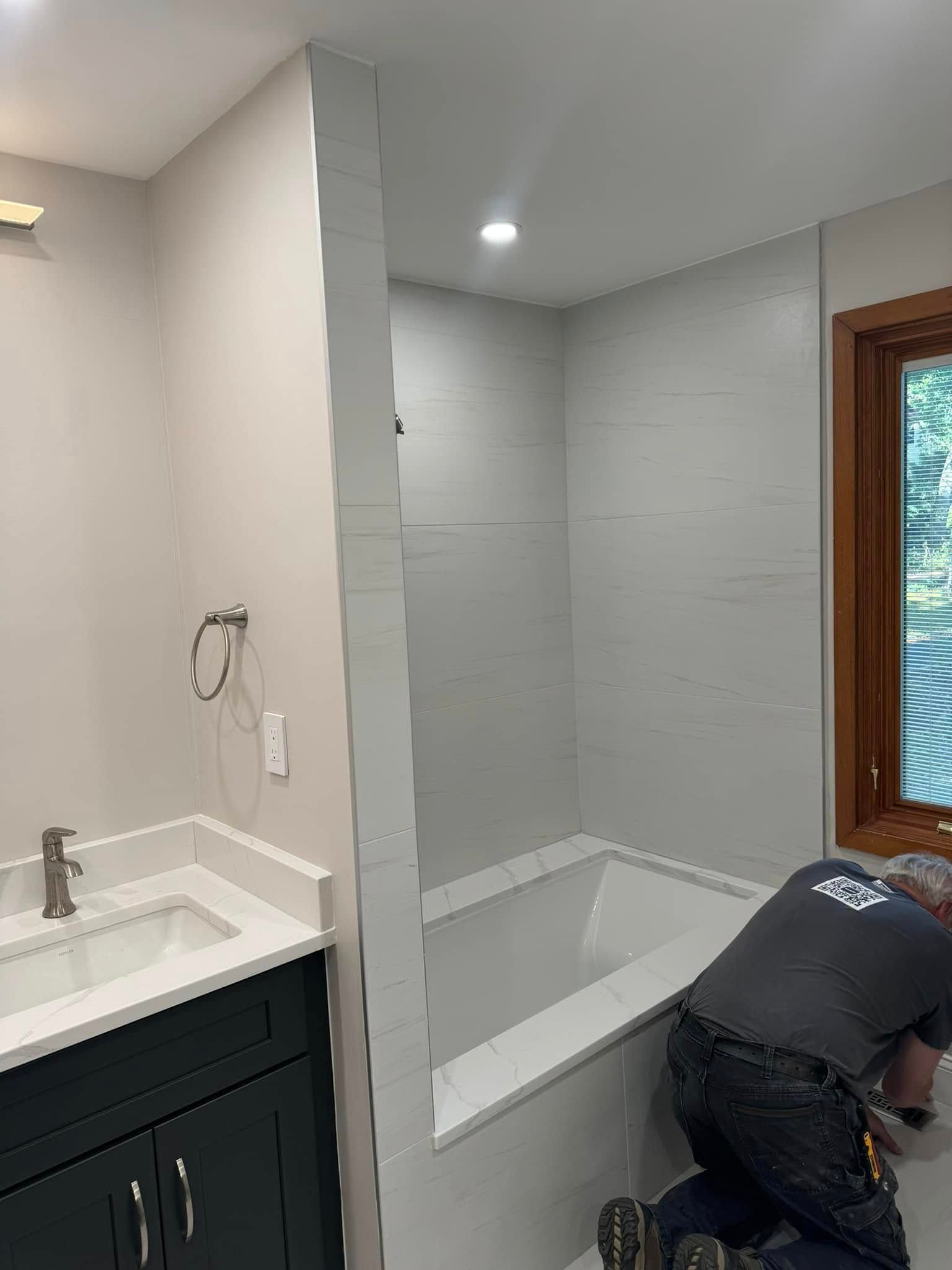 Bathroom with tiled shower and tub, worker installing tile.