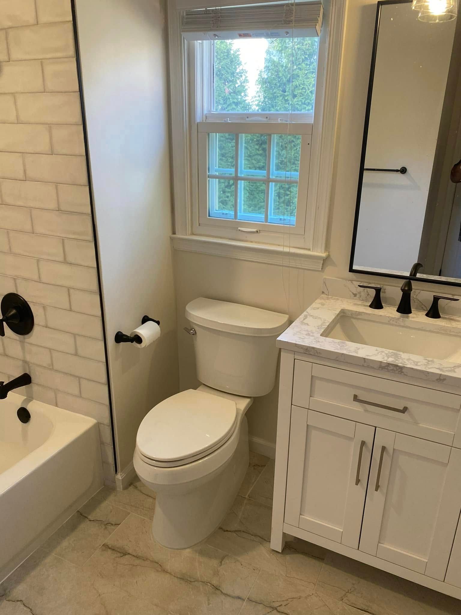 Bathroom with white toilet, vanity, and brick-style tiled wall; window with natural light.
