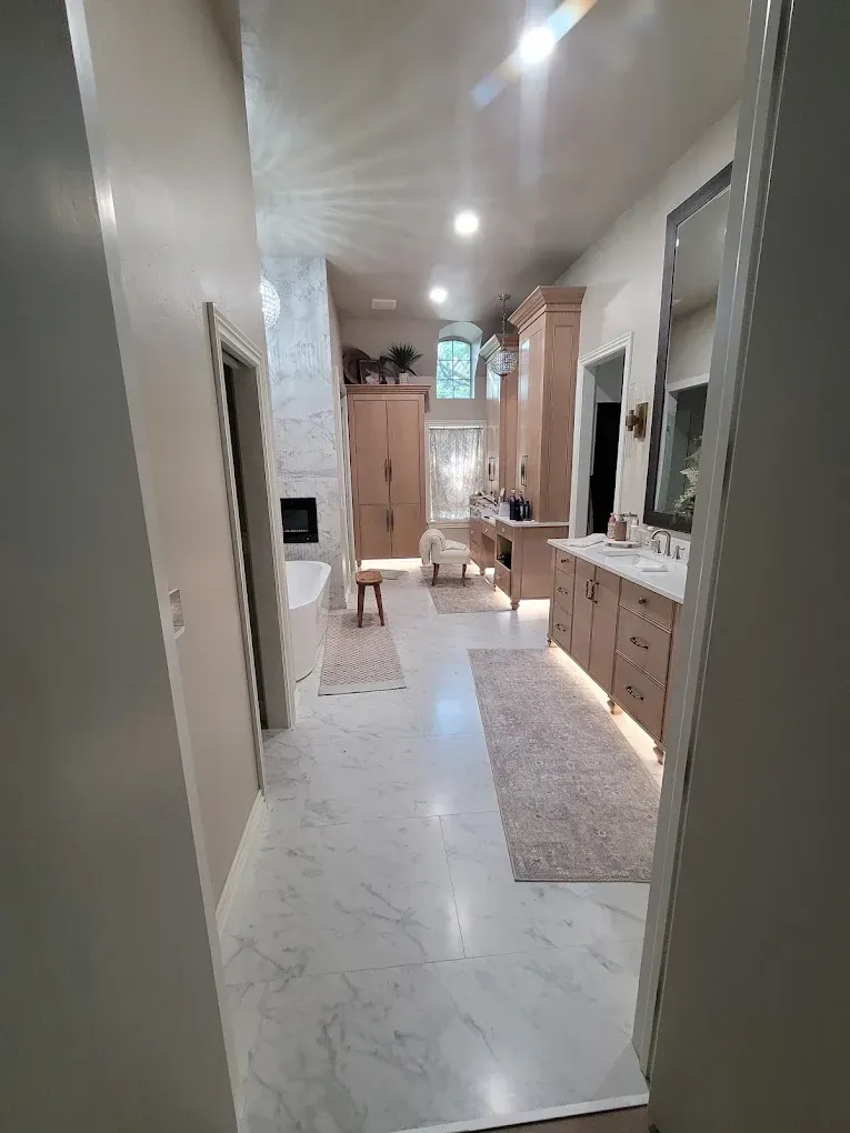 Spacious, light-filled bathroom with marble floors, double vanity, and a fireplace.