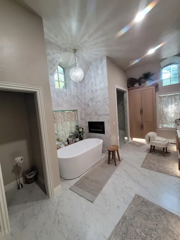 Spacious bathroom with a freestanding tub, faux marble walls, wood cabinet, and ornate chandelier.