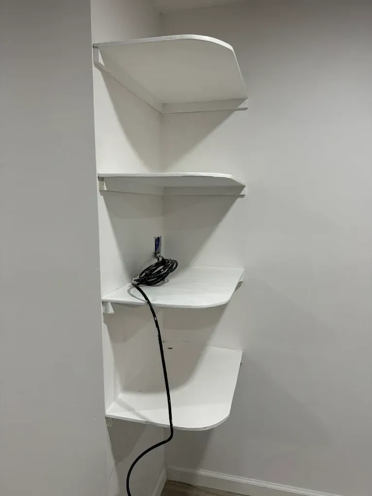 White corner shelves with a black cord on a white wall.