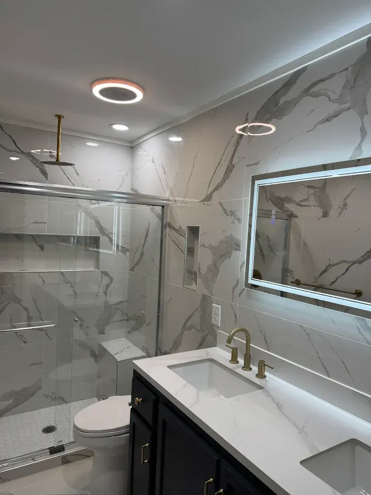 Modern bathroom with marble tile, glass shower, vanity, and circular ceiling lights.