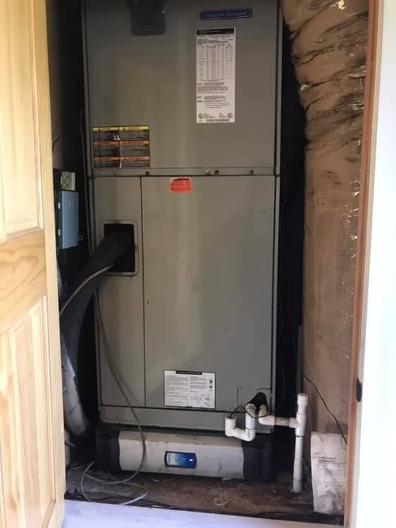 HVAC unit in a closet. Gray metal appliance with pipes and wires. Light wood doorframe.