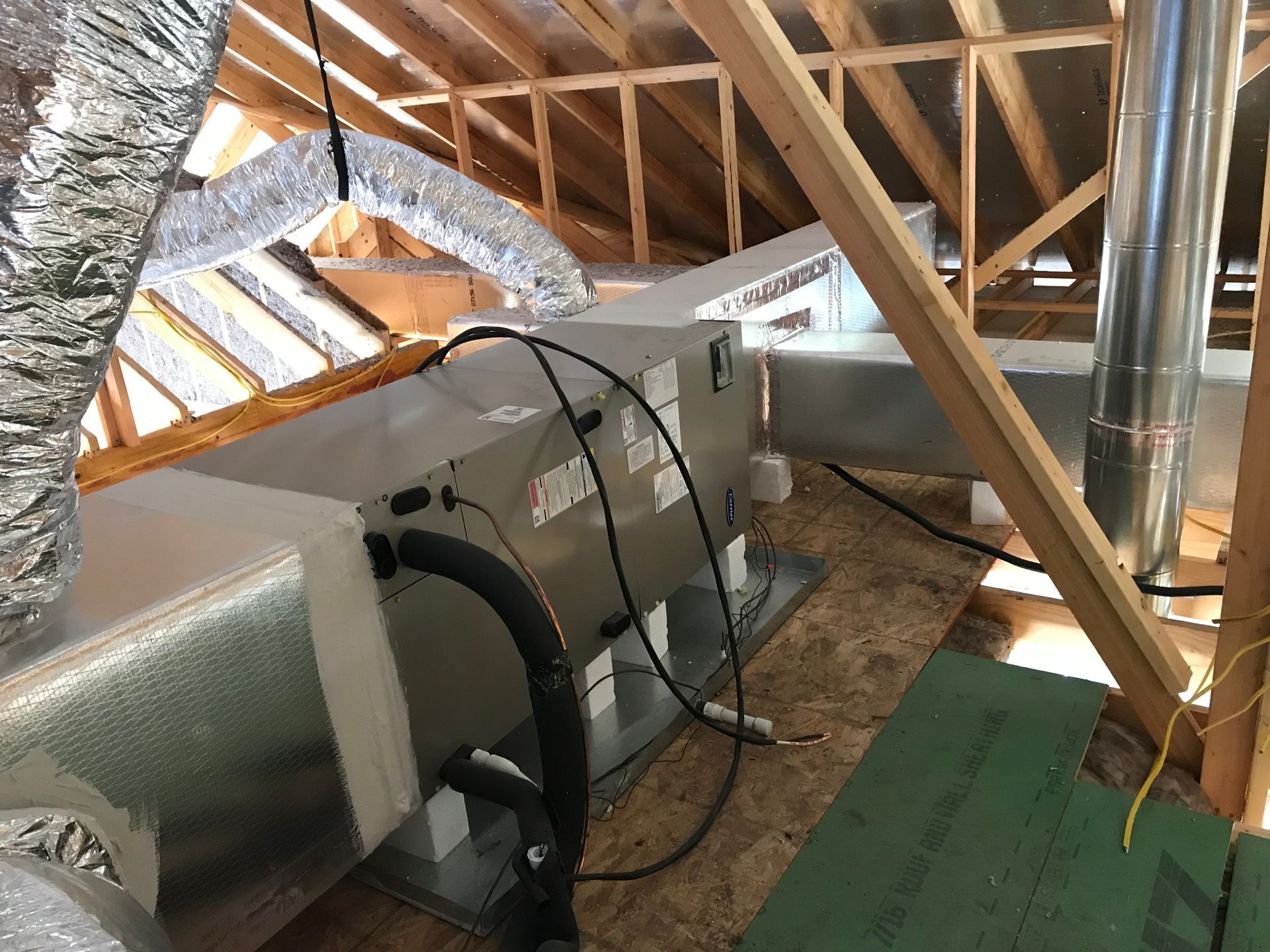 HVAC unit installed in a wooden attic, with ductwork and plumbing.