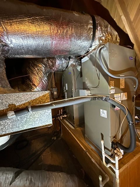 HVAC unit in an attic with insulated ductwork. Silver and gray components in a confined space.
