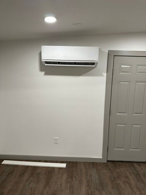 White air conditioning unit on a white wall in a room with a closed door.