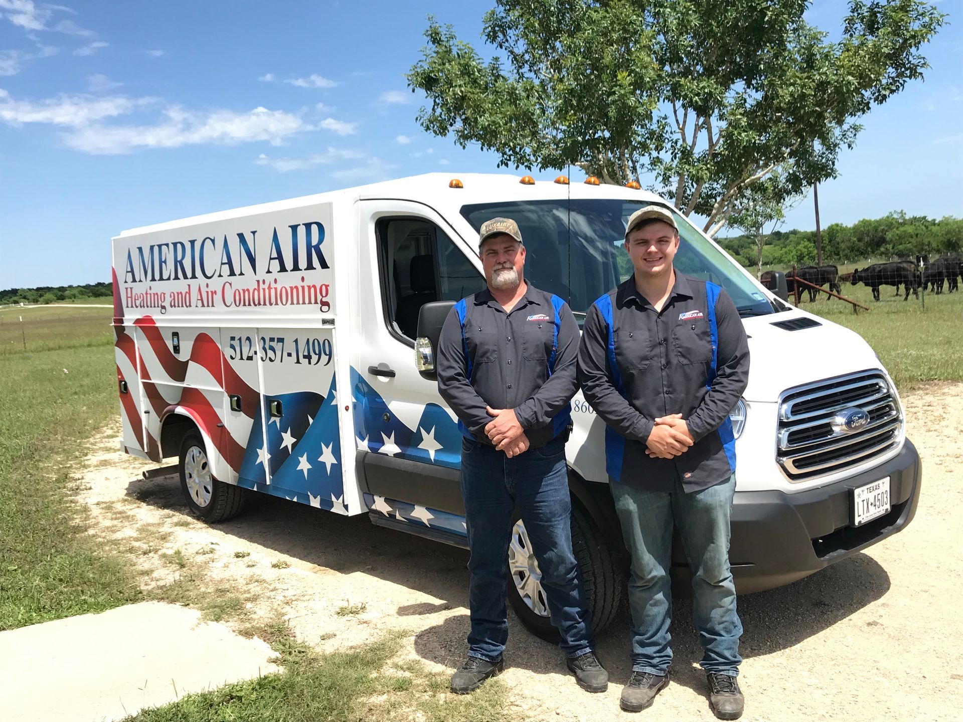 Two men in work shirts pose beside a white van with an American flag design.