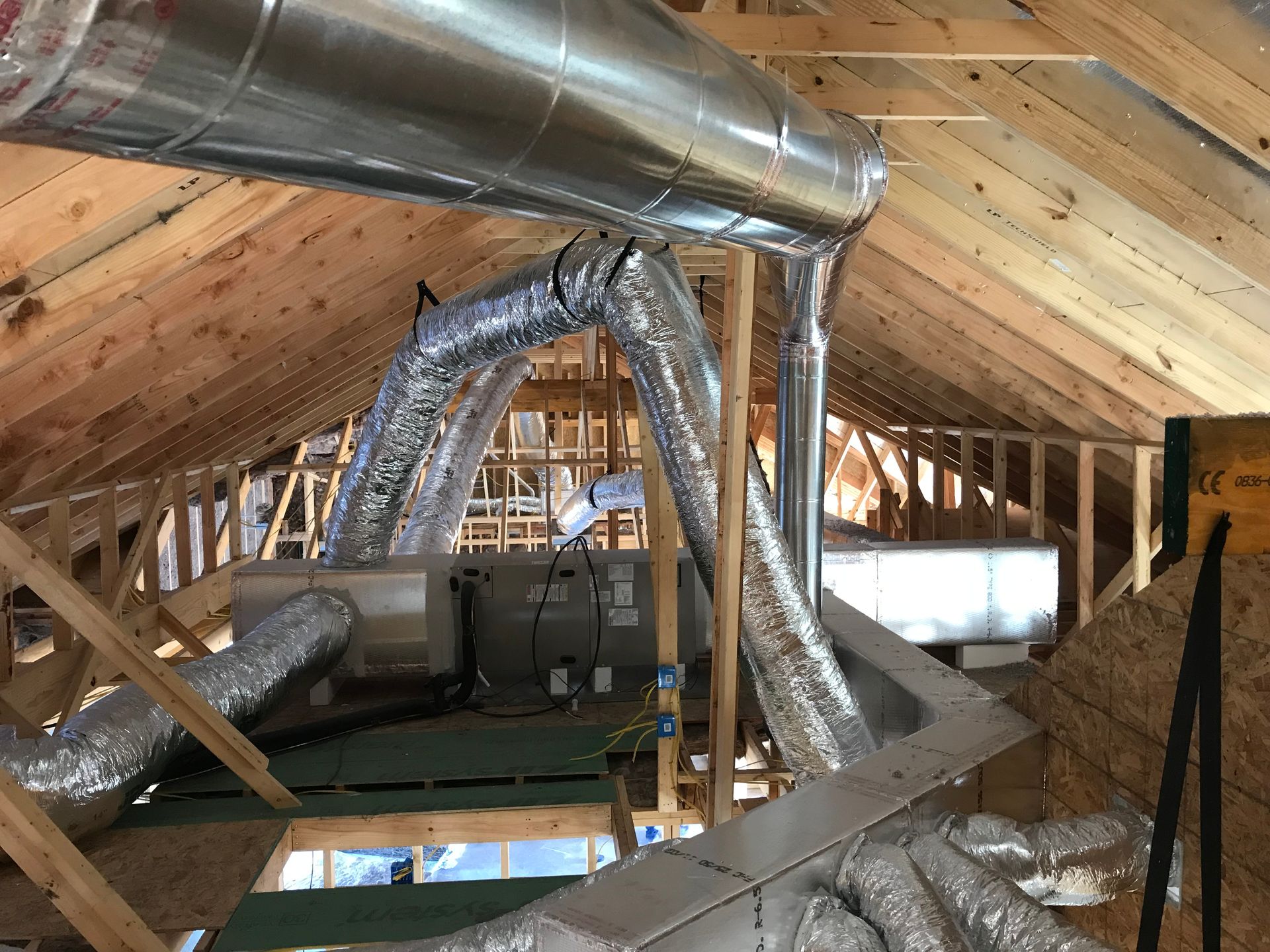 HVAC ductwork installation in an unfinished attic space, with silver flex and rigid metal ducts.