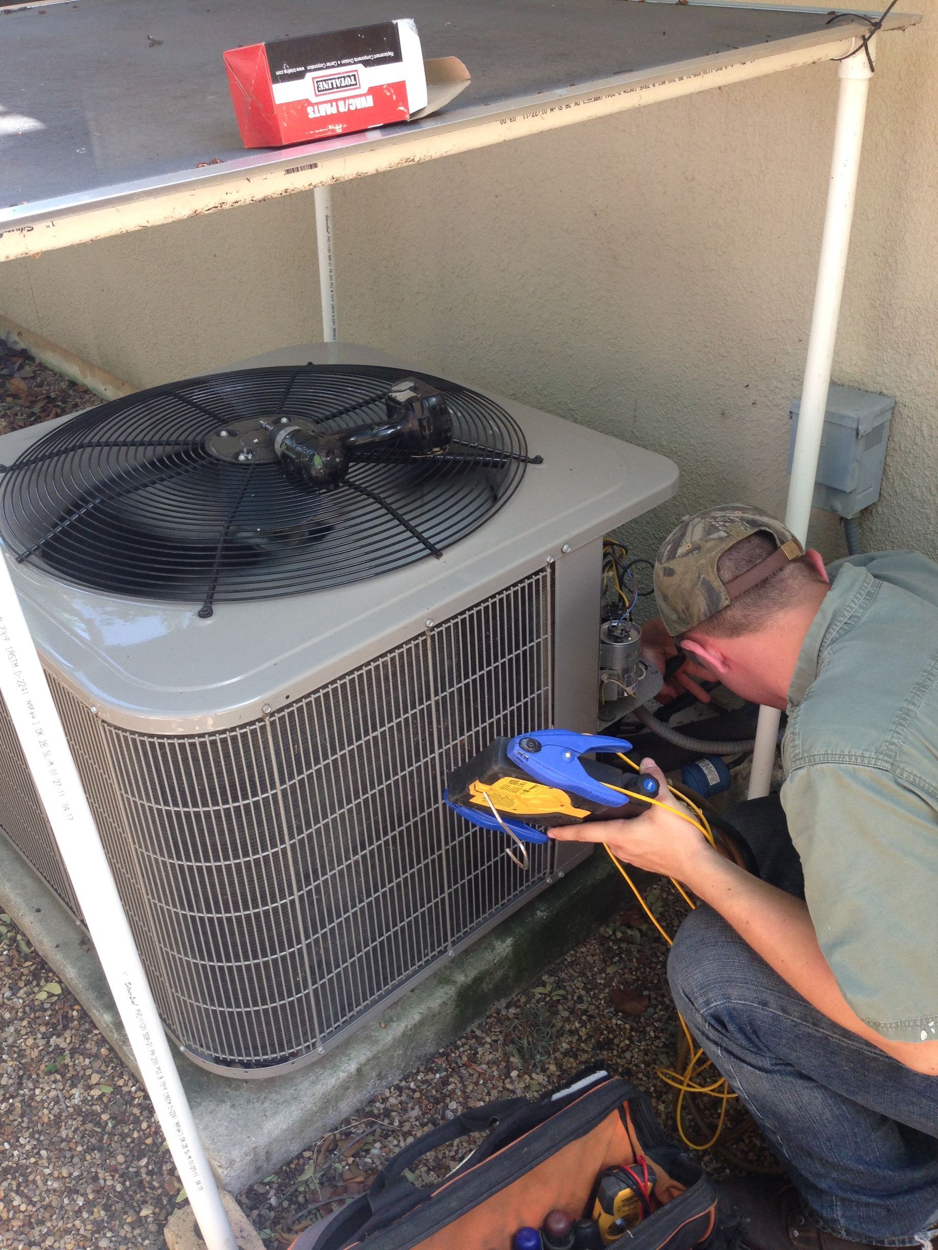 Man examining an AC unit with a flashlight outside a house.