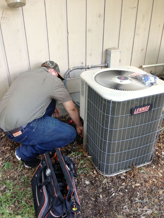 HVAC technician crouching near an air conditioning unit outside a building, working on the components.