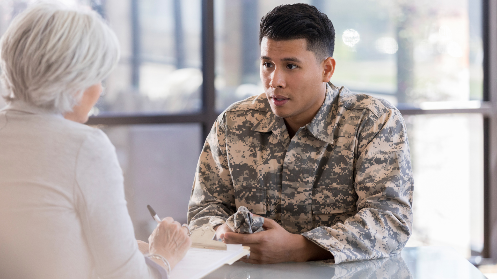 A soldier is sitting at a table talking to a woman.
