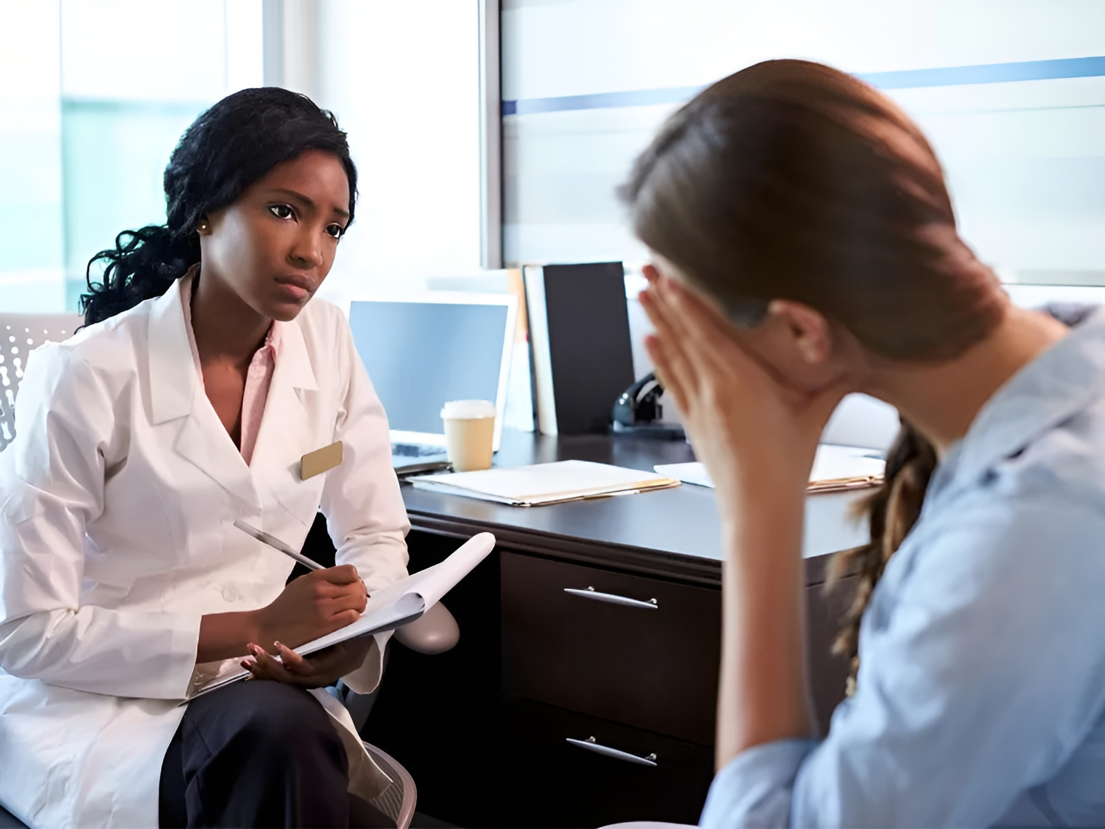 A doctor is talking to a patient who is covering her face with her hands.