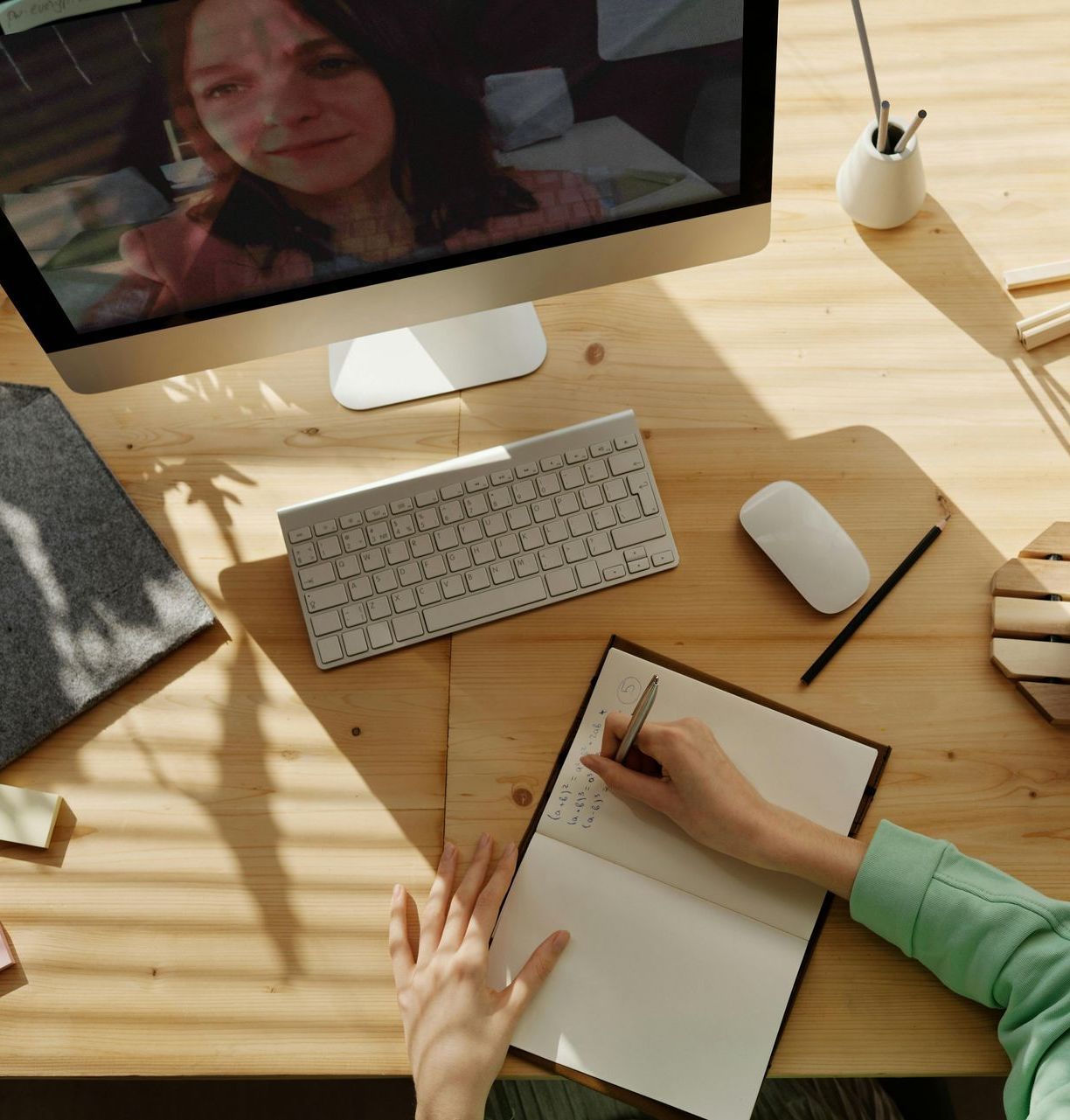 A person is writing in a notebook while looking at a computer screen
