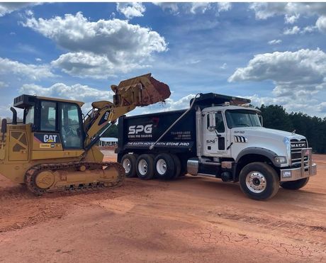 One of Stone Pro Grading, LLC's dump trucks and bulldozers in a dirt field.