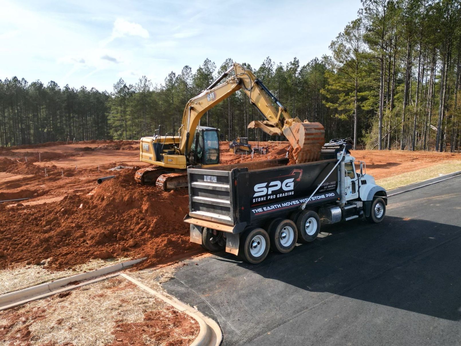 Stone Pro Grading, LLC's dump truck is being loaded with dirt by an excavator.