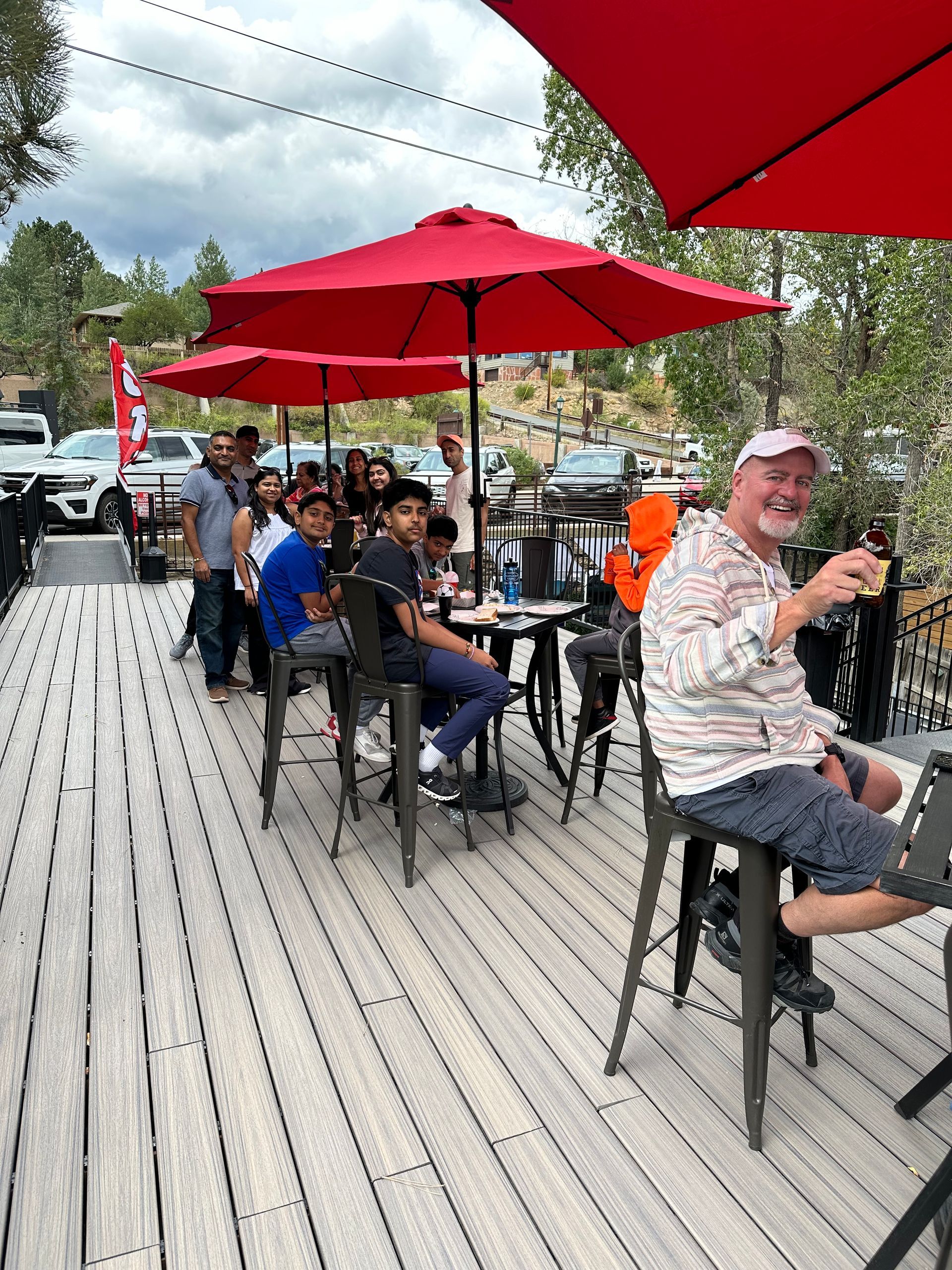 A group of people are sitting at tables under red umbrellas on a deck.