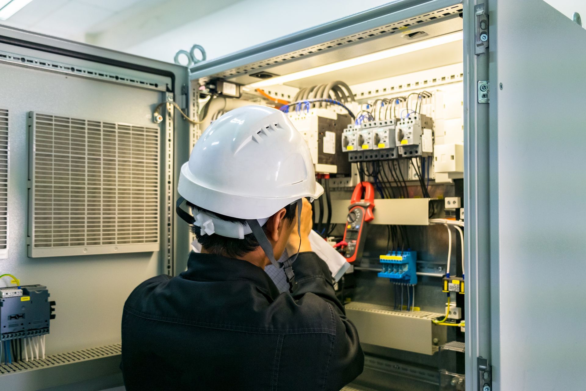 A man wearing a hard hat is working on an electrical box.