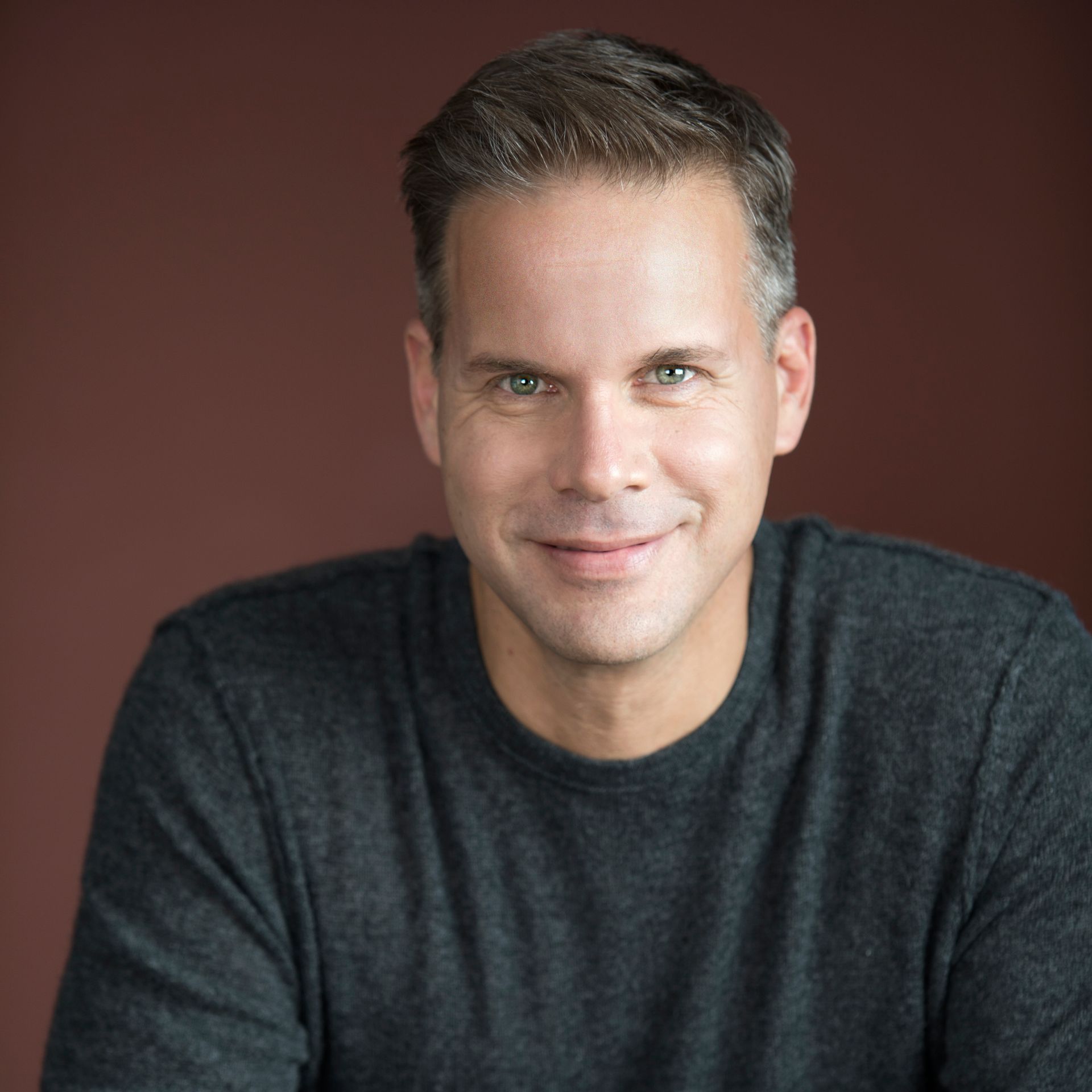 A man in a grey shirt is smiling for the camera.