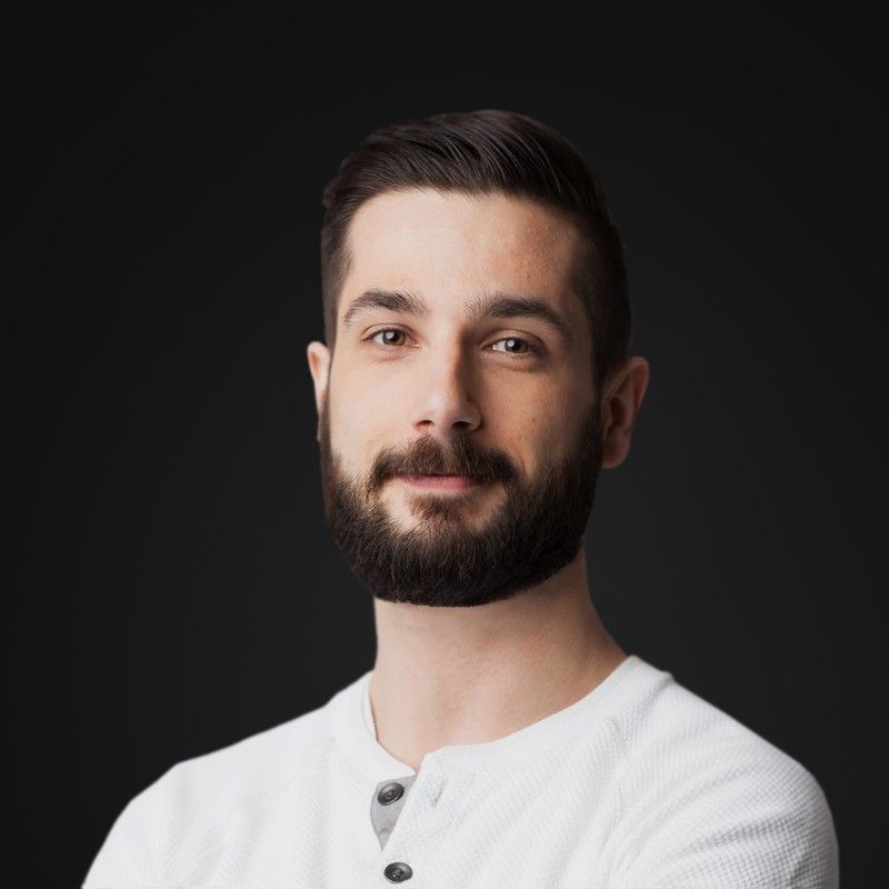 A man with a beard is wearing a white shirt and has his arms crossed.