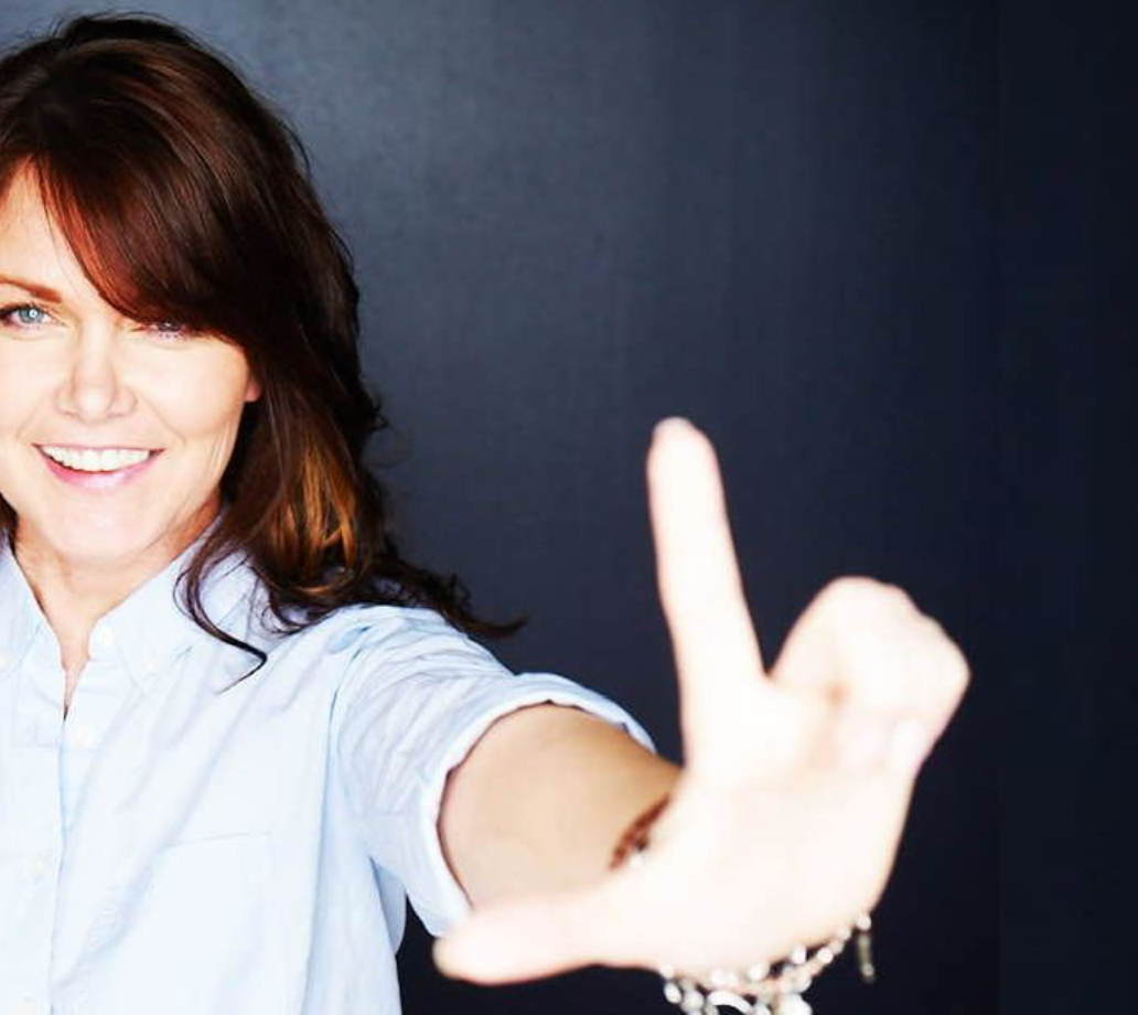 A woman in a blue shirt is smiling and making a thumbs up sign