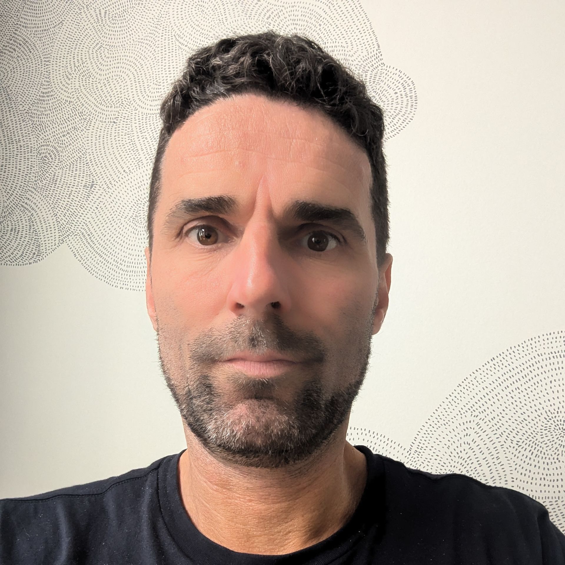 A man with a beard is wearing a black shirt and looking at the camera.