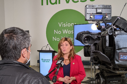 A woman in a red jacket is talking to a man in front of a camera.