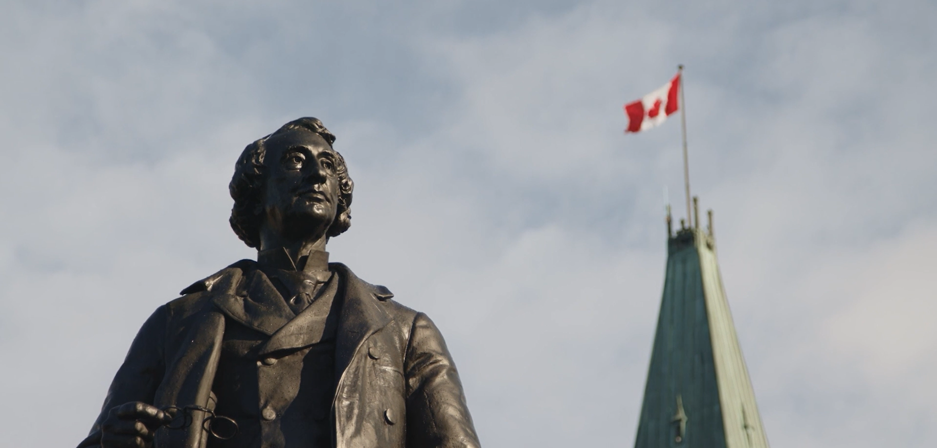 A statue of John a Macdonald with a canadian flag in the background