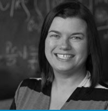 A black and white photo of a woman smiling in front of a chalkboard.